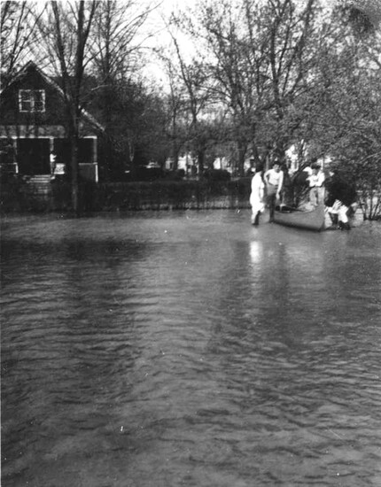 Residents sit in and stand around a small wooden boat outside their home at 76 Crocker Boulevard (later 60 Crocker) during flooding at Third Street in 1946.