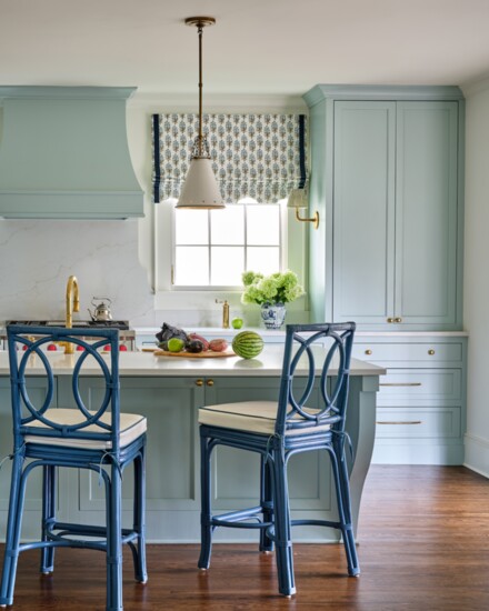 Bright blue counter stools by Mainly Baskets line the kitchen island. Roman shade fabric is Jangali by Bastideaux.