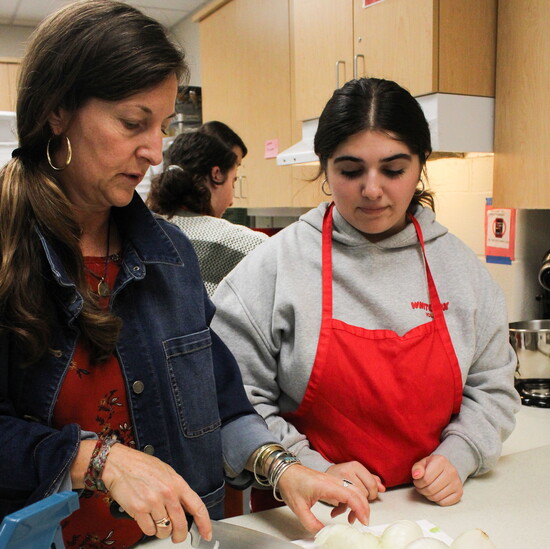 Rachel Pangu assists students with knife skills while dicing onions