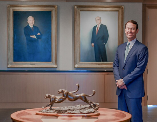 Powell Brown in front of portraits of Hyatt and Adrian Brown. (Photo Credit: Brown & Brown)