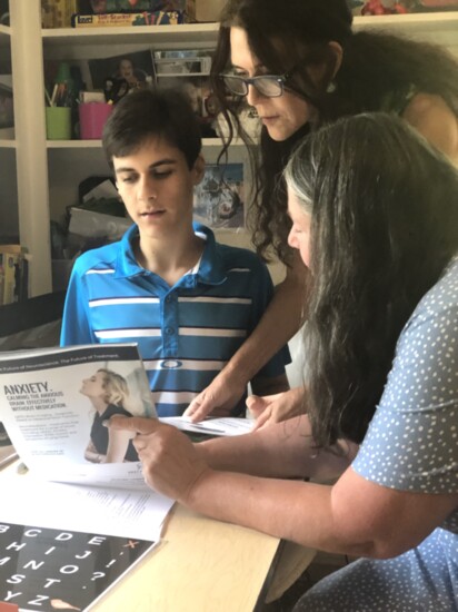 Wynston's mother, Lynda, and communication partner, Elisa, show Wynston an issue of Westport Lifestyle Magazine.