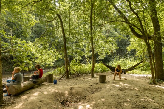 Parker Morris and Oliver Holdsworth eat lunch on a log while Nova Hitchcock sits in a hammock.