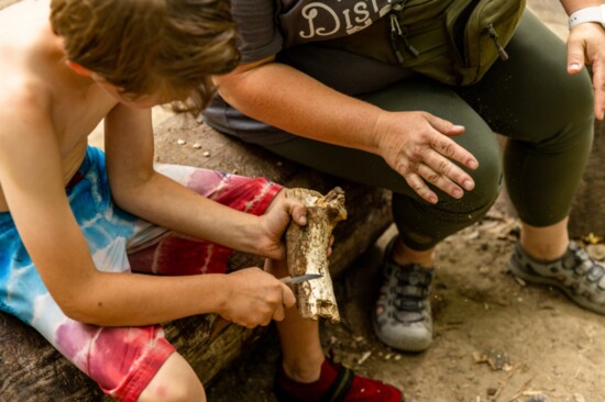 Elementary Assistant Teacher Meghan Davis Van Tol, right, talks Liam Anderson, left, through the proper technique in whittling a piece of wood with a knife.