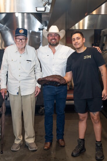 John Tommey, grandson, Charles, and a brisket hot off the pit displayed by a grill master. 