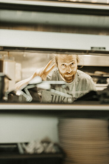 Jake Jukes runs the backline at Jukes Ale Works, flashing a peace sign from the kitchen pass