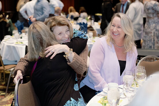 Lynn Neil gives a hug while Valerie Scoggin smiles in celebrating at the 2025 Lunch for LiteracyPC: Lynnsey Phillips