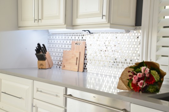 The polished chrome backsplash is complemented by the light gray quartz countertop. Note the under-cabinet modular power strip installation.
