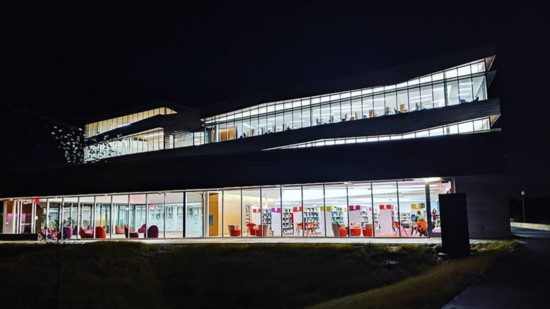 Lights shine out to the night sky from the south side of Norman Public Library Central as readers use the children’s services area on the first floor.