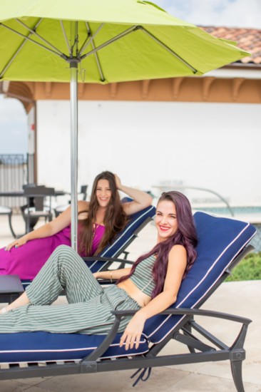Sisters Lauren and Morgan Maness lounge poolside. Lauren is wearing a purple dress from Briesly's Boutique, and Morgan is wearing a pant set from Hello Daffodil
