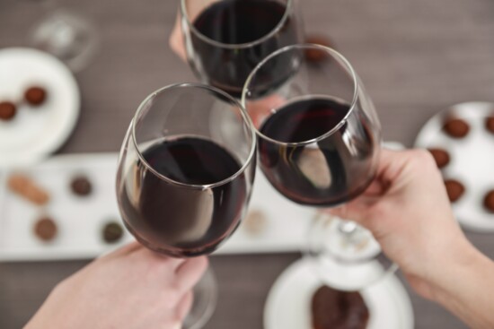 People toasting glasses of wine over chocolates.