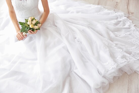 Person sitting in wedding dress with a bouquet.