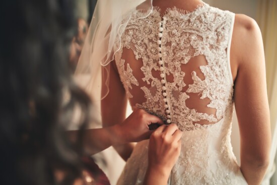 Person helping bride with a dress.