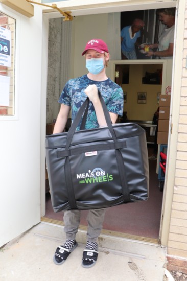 Volunteer, Tyler Chase, carries a bag loaded with meals to the cars.