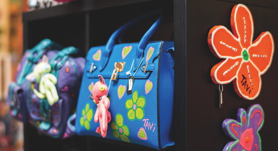 Hand-painted handbags and accessories showcase TAVi's playful designs, each one-of-a-kind piece transforming everyday items into wearable art.