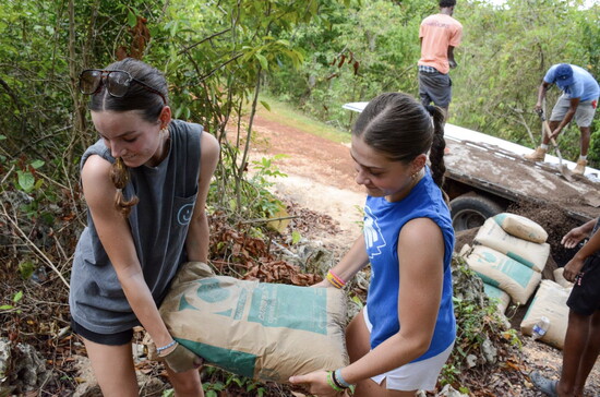 Keileen Burt and Madi Hamblen haul cement mix up the mountain at the house worksite.