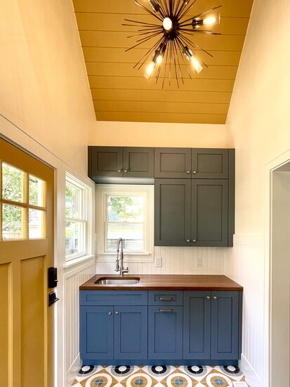 Patterned concrete tile was the inspiration for this mudroom. Painted cabinets and a butcherblock countertop are jazzed up by the paneled mustard ceiling and do
