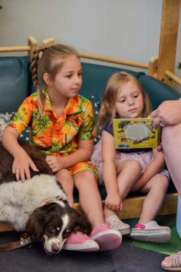 Two sisters sit alongside PAWS therapy dog Lucky as their mom reads a classic book.