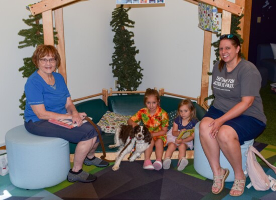 A dedicated PAWS for Reading volunteer and her certified therapy dog, Lucky, pose with a mother and her two daughters, regular participants of the program.