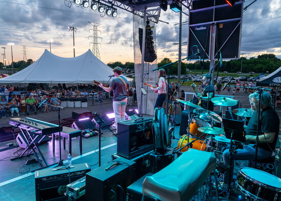 Stage lights illuminate the band as the sun sets over Veterans Park.