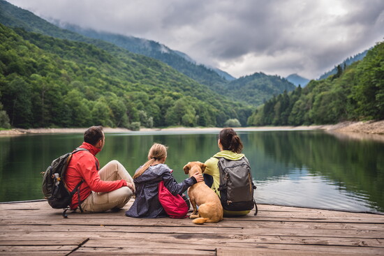 Family with a dog sitting alongside the water.