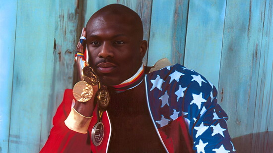 Steve Lewis as a young athlete, proudly holding his Olympic medals, outfitted in the stars and stripes.