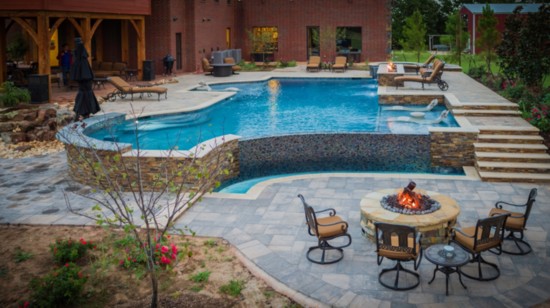 Modern design pool with swim-up bar, negative edge, raised wall with fire feature. Straight and curved lines add style.