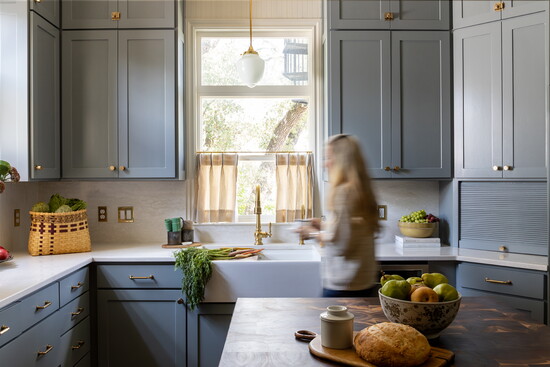 Custom blue cabinets, brass elements, creamy quartz countertops, and the touch of farmhouse in the curtains perfectly blend the old with the new.