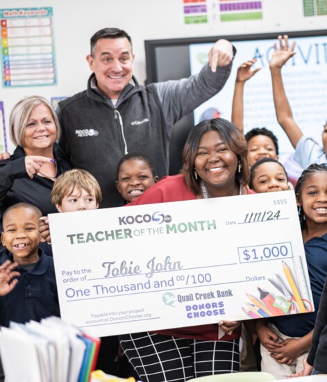 A teacher is all smiles as she is presented with a check as KOCO and Quail Creek Bank Teacher of the Month.