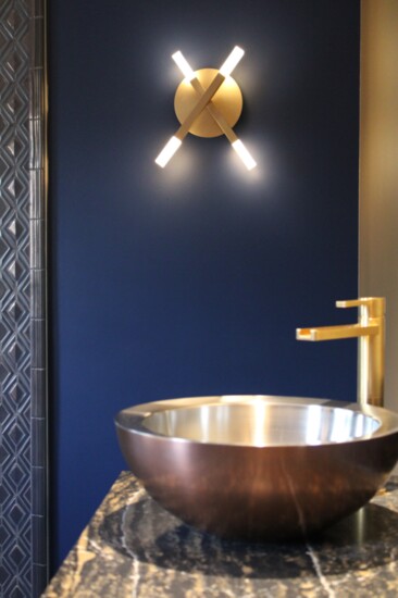 Copper vessel sink with gold waterfall faucet and luxury matte black, gold, and white quartz countertop.