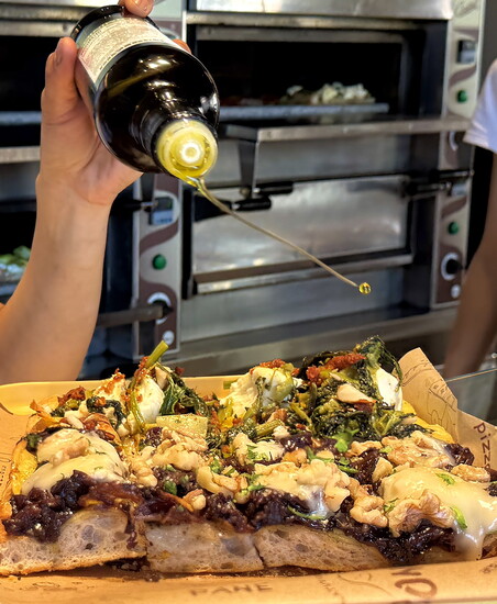 A splash of olive oil finishes a slab of pizza al taglio, cut with scissors and sold by the pound, at Pizzarium Bonci in Rome’s Trionfale district.