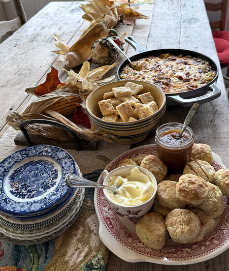 A table scape of flaky layers of buttermilk biscuits, overnight slow cooker apple butter, biscuit crackers, Sausage Balls and Bacon Spinach Artichoke Dip