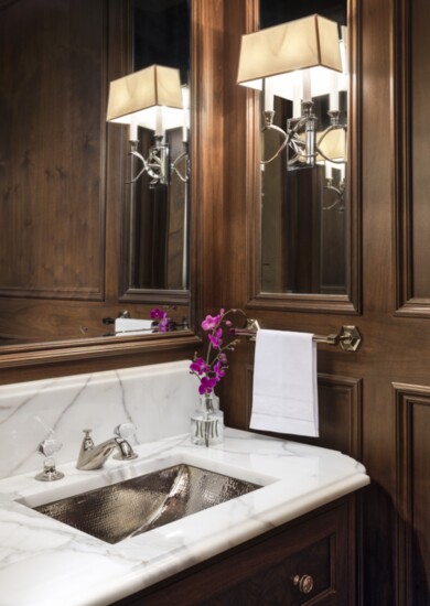 “The formal powder room’s walls are paneled in gorgeous walnut, with an inset mirror and metallic ceiling,” Rasschaert says. The Waterworks faucet is embellishe