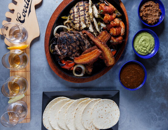 A vibrant spread at Tiho’s Tequila Bar & Restaurant, featuring grilled meats, fresh tortillas, and flavorful sauces, perfect for sharing and savoring.