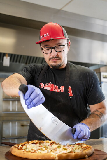 Hot out of the oven: slicing up a specialty Roma pizza loaded with toppings.