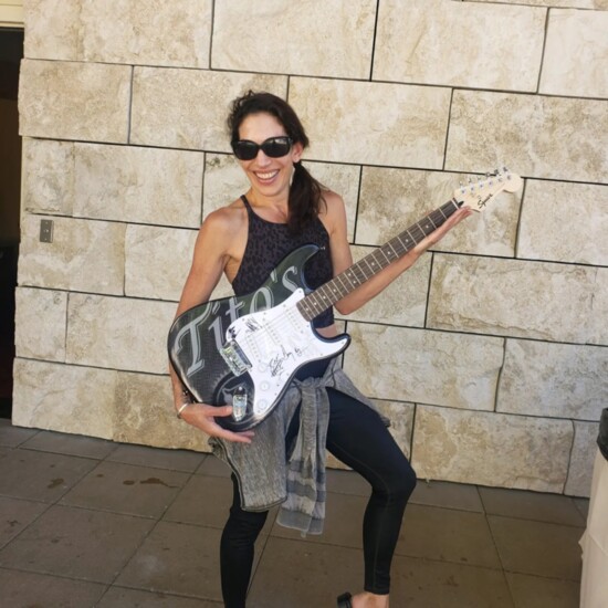 Jenn Terra holds a Tito's Handmade Vodka electric guitar signed by The Marshall Tucker Band as a donation item for fundraising at a Sun Valley Pavilion concert