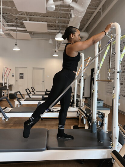 A BODYBAR Woodforest member works through a standing resistance sequence on the reformer.