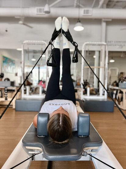 A member practices controlled leg work in straps during a reformer session at BODYBAR Woodforest.
