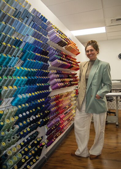 Johnson stands beside the extensive thread collection at Fit & Style, showcasing the craftsmanship tools behind her boutique's operations.