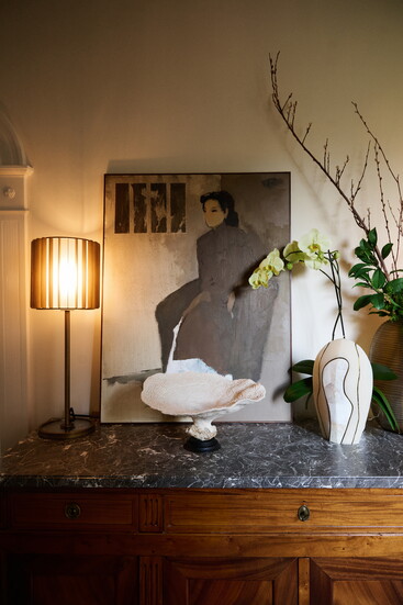 An antique marble-topped commode from CIIRCA Antiques is paired with a coral-footed sculpture also from CIIRCA, alongside a portrait from the client’s personal 