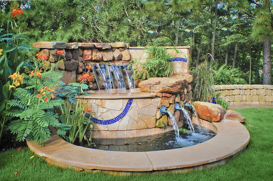 A stone waterfall feature adds motion and sound while tying planting, hardscape, and water into one cohesive backyard focal point.