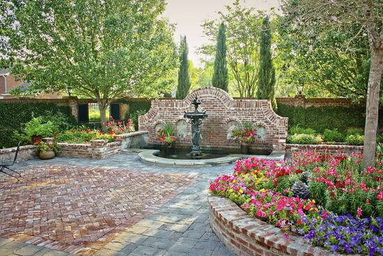 Brick paving, layered color, and a central fountain create a formal courtyard that boosts value through structure, symmetry, and year round beauty.