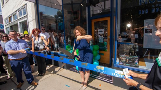 Michelle Moog-Koussa cutting the ribbon at the Moogseum with city officials holding the ribbon.