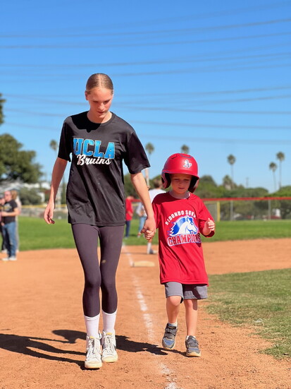 Buddy and athlete hand in hand heading to home plate.