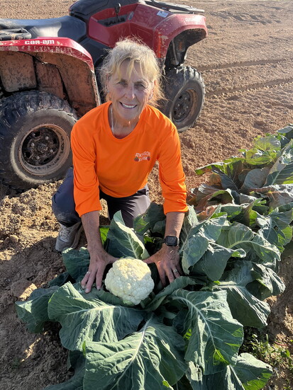 Theresa Atkinson shows a cauliflower before picking for harvest.