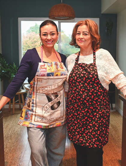 Gia and her mom don smiles and aprons in the kitchen.