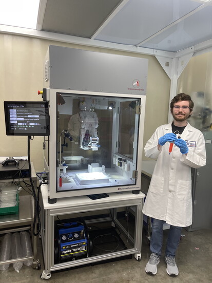 Samuel Hopkins standing next to the Bioassembly Bot, a six-axis robotic arm bioprinter capable of printing large and complex biological structures. 