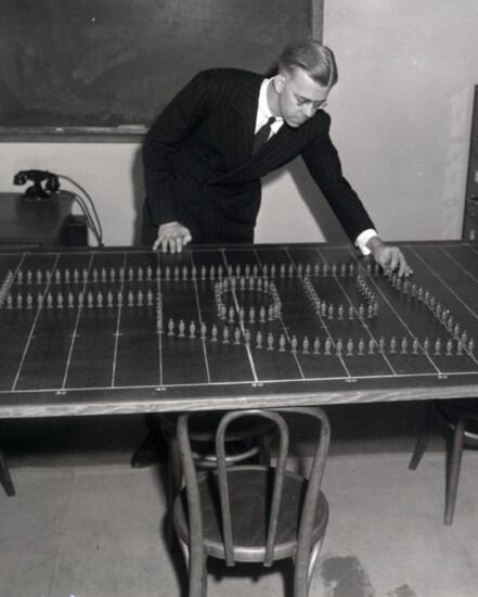 Band director Leonard Haug (1945-62) choreographs band moves on a scale model football field. (Courtesy University Libraries Western History Collections)