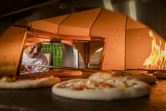 Chef Hany overseeing pizzas in the wood burning oven at Mercato di Vienza.  Try one from the menu or create your own!