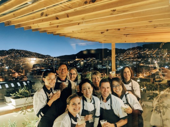 Taste of Peru travelers enjoying a Pisco sour after a cooking class, with the lights of Cusco behind them.