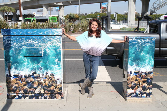 Kerry stands between utility boxes wrapped with her ocean jetty photography in Redondo Beach.